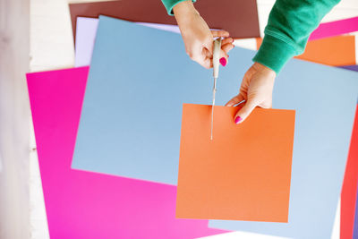 Cropped hands of woman cutting orange kraft paper on table
