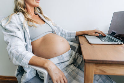 Unrecognizable pregnant woman working at home online.