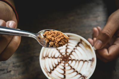 Cropped hands on person adding brown sugar in coffee at table
