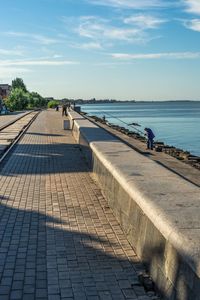 People on footpath by sea against sky