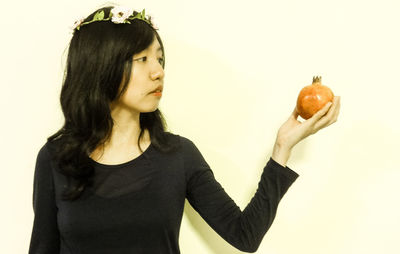 Woman wearing wreath looking at pomegranate against wall