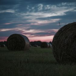 Hay bales on field against sky during sunset