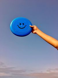 Cropped hand holding plastic disc against sky