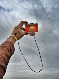 Low angle view of cropped hand against cloudy sky