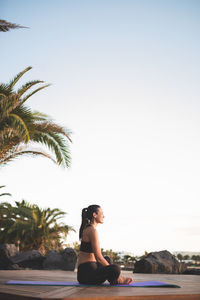 Side view of woman sitting on beach against clear sky