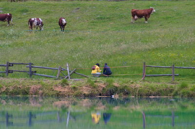 A couple reflected on lake with a farm in background 