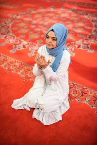 High angle view of young woman praying while sitting in mosque