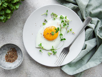 Fried eggs, microgreens and spices on a white plate on concrete background