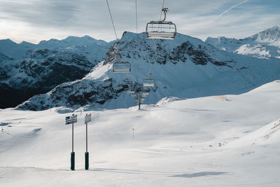 Empty ski lift against snow covered mountains and sky