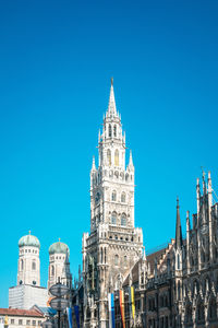 Low angle view of new town hall by munich cathedral against clear blue sky