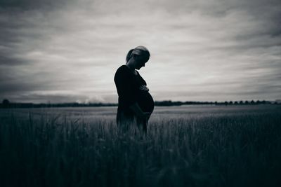 Man standing on grassy field against cloudy sky