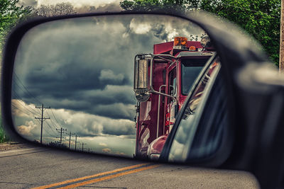 Firefighter truck against cloudy sky reflecting on car side-view mirror