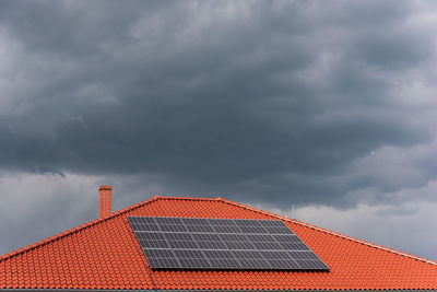 Red tile roof with photovoltaic panels during stormy weather, solar pv installation dark blue clouds