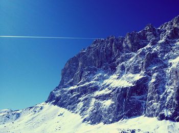 Low angle view of snow covered mountain against blue sky