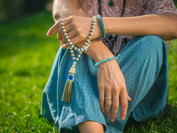 Midsection of woman with bead jewelry sitting on grassy field