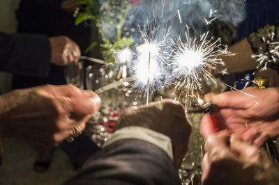 Cropped hands of people holding illuminated sparklers at night
