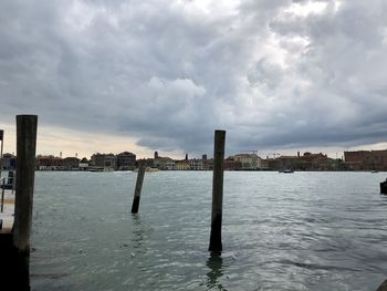 Wooden posts in sea against sky in city