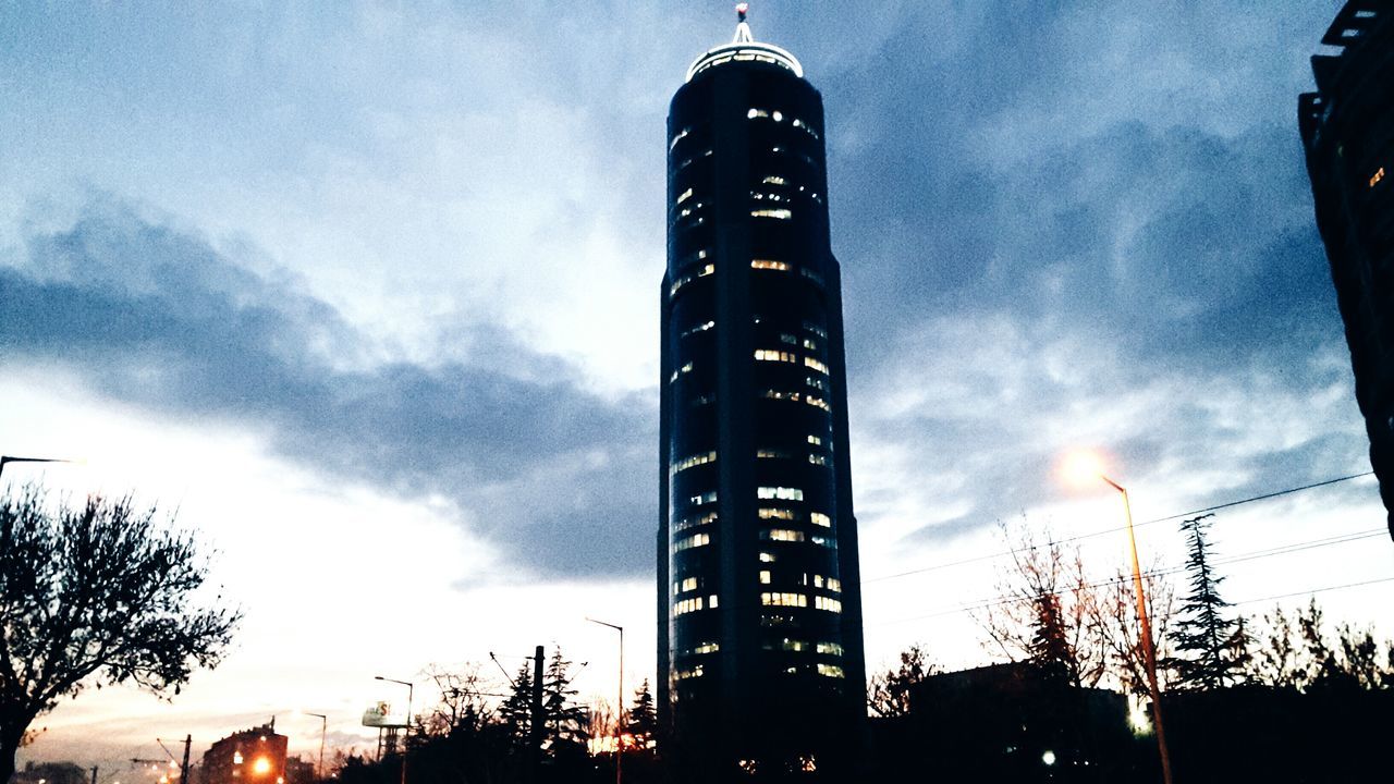 low angle view, sky, built structure, tall - high, architecture, cloud - sky, tower, building exterior, silhouette, city, dusk, sunset, communication, tree, skyscraper, illuminated, cloudy, cloud, modern, street light