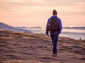 Rear view of man standing on land against sky during sunset