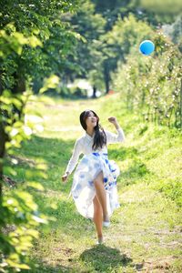 Full length of happy woman catching balloon while running on grassy field in park