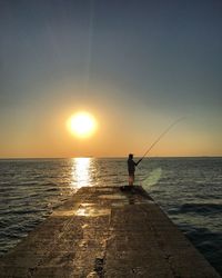 Silhouette man fishing in sea against clear sky during sunset