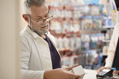 Pharmacist reading instructions on medicine box at pharmacy store