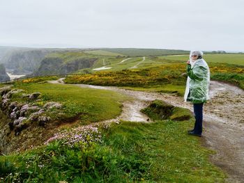 Side view of man wearing raincoat while standing on mountain against sky