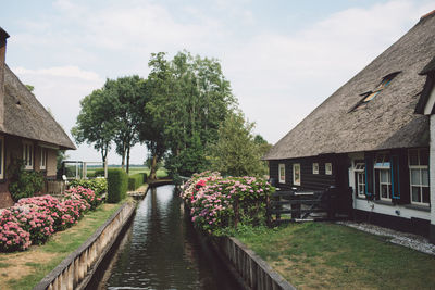 Scenic view of canal amidst houses and trees against sky