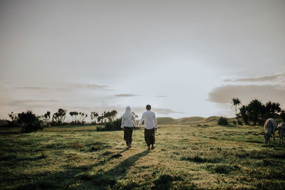 Rear view of men walking on field against sky