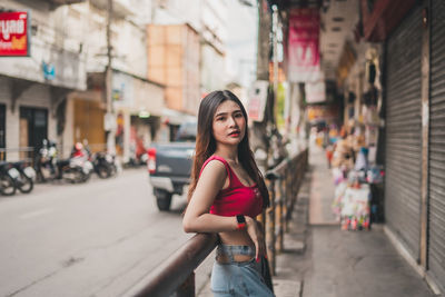 Portrait of woman standing by railing in city