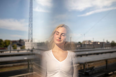 Double exposure image of young woman with railroad tracks against sky