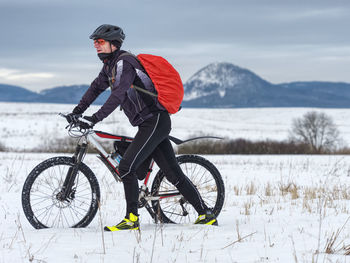 Adult biker pushes mountain bike through snow across frozen meadow. hard terrain, biker can't ride.