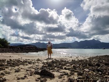 Rear view of woman standing on beach against sky