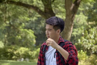 Portrait of young man looking away against trees