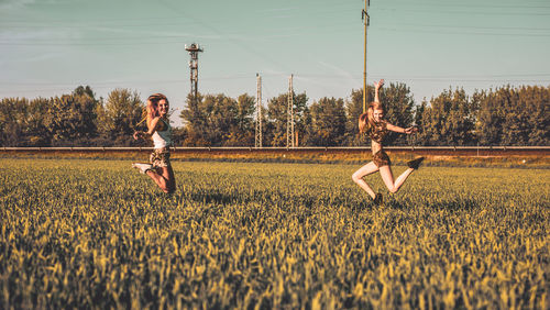 Friends jumping on grassy field against sky