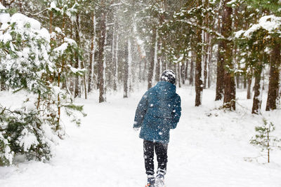 Back view of child boy in winter forest in snowstorm. actively spending time outdoors. winter snowy