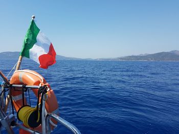 Italian flag and life belt hanging on boat in sea against clear sky