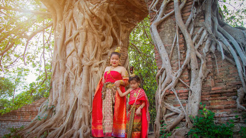 Asian girl in a thai dress walk with her mother from an old brick gate with a big root tree 
