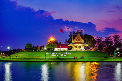 Illuminated building by lake against sky at dusk