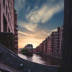 Buildings by river against sky during sunset