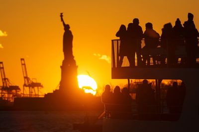 Silhouette people standing by sea during sunset