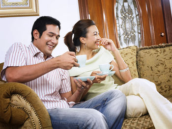 Smiling mid adult couple drinking coffee on sofa at home