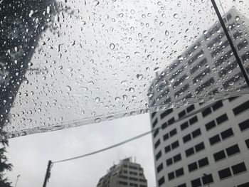 Low angle view of buildings seen through wet glass window