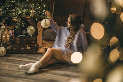 Young woman with headphones listens to music from vinyl record, sitting on floor near christmas tree