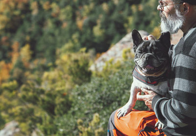 Closed image of a man sitting with dog on a rock looking at the landscape on the mountain cliff