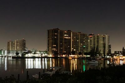 Illuminated buildings by river against sky at night