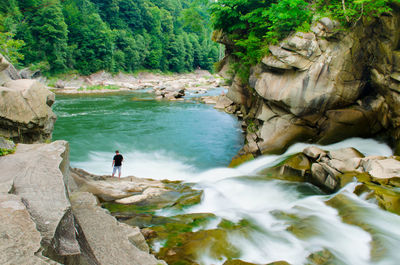 High angle view of man standing on rock by waterfall at forest