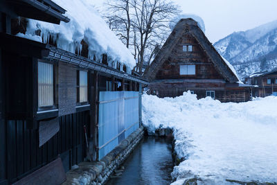 Snow covered houses by frozen lake against sky