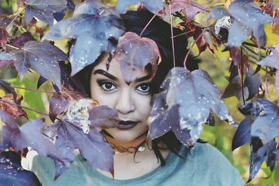 Portrait of beautiful woman peeking through maple leaves during autumn