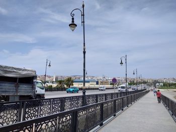 Street lights on bridge in city against sky